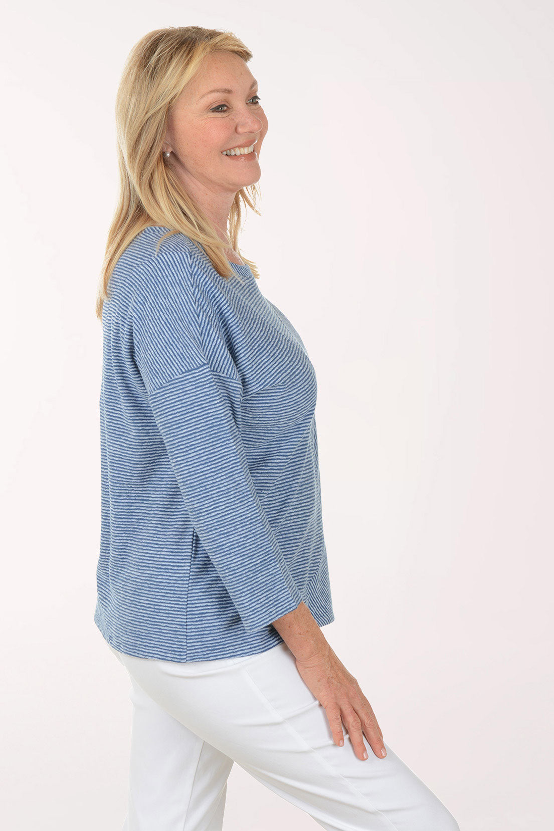 Woman wearing a blue striped sweater and white pants on a white background