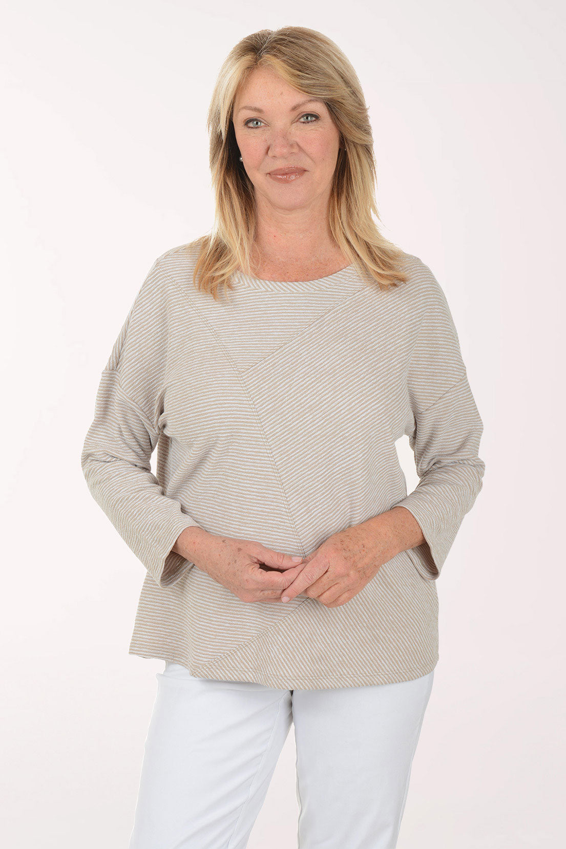Woman wearing a beige sweater and white pants on a light pink background