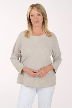 Woman wearing a beige sweater and white pants on a light pink background