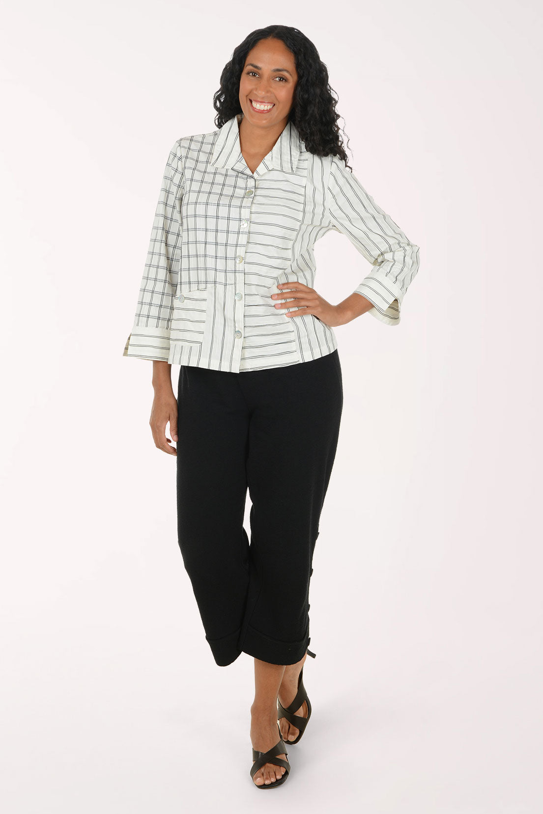A woman modeling a light green and white striped button-down blazer with black cropped pants and black sandals, standing against a plain white studio background.