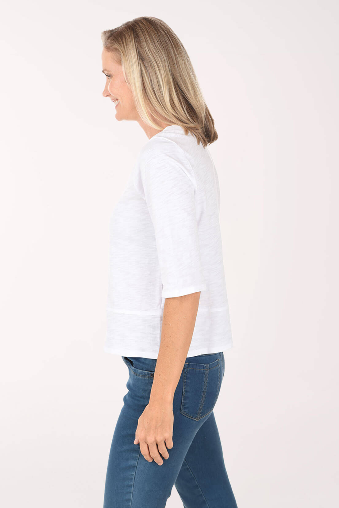 Woman wearing a white shirt and blue jeans on a white background. Side shot