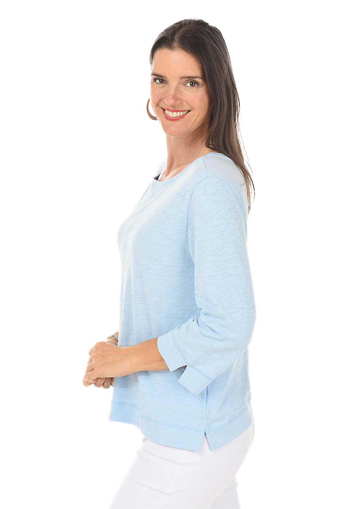 Woman wearing a light blue top and white pants on a white background. Side shot.