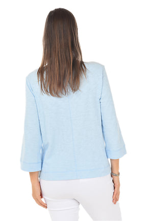 Woman wearing a light blue top and white pants on a white background. Back shot.