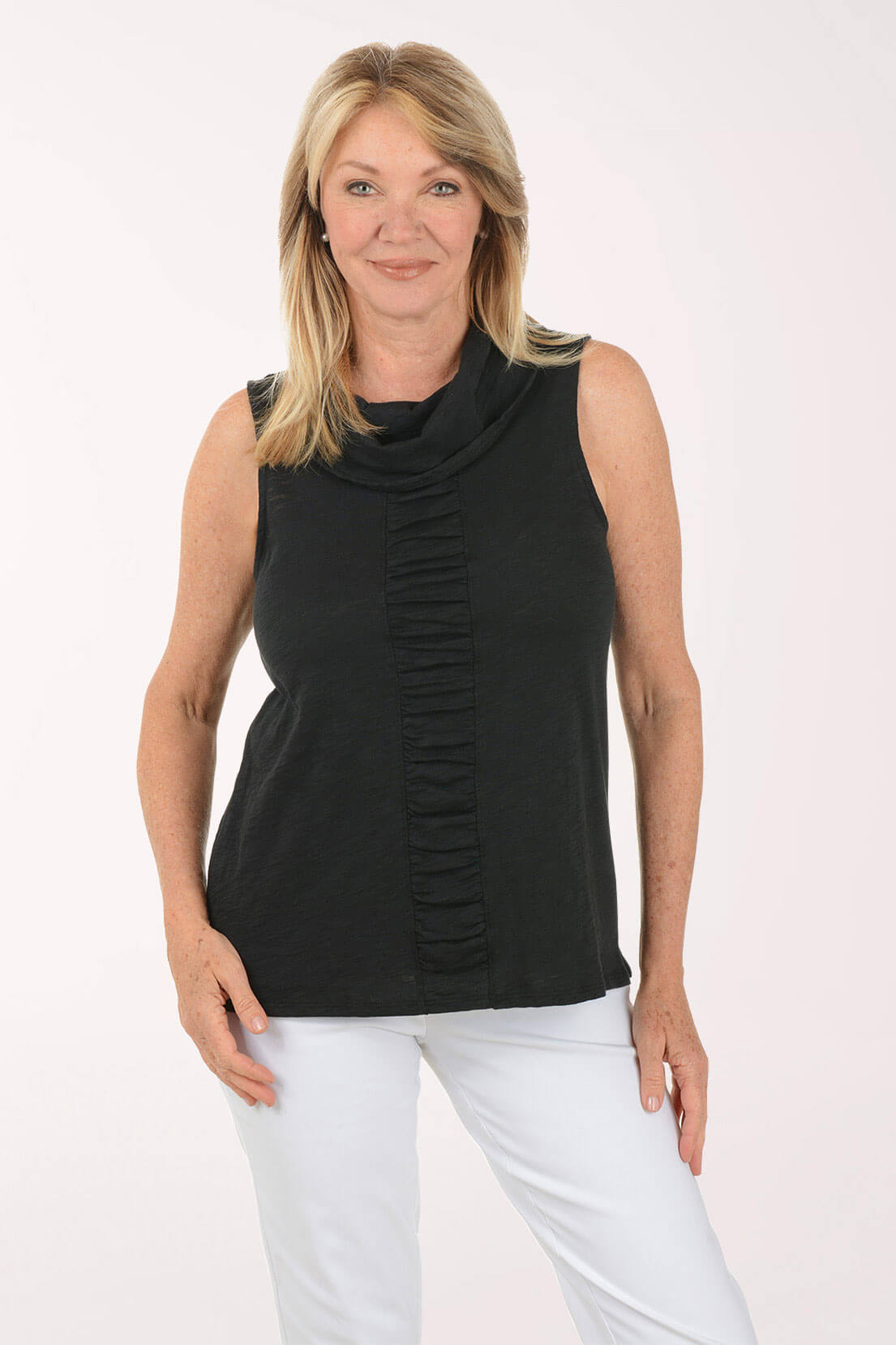 Woman wearing a black sleeveless top with a ruched design and white pants on a white background