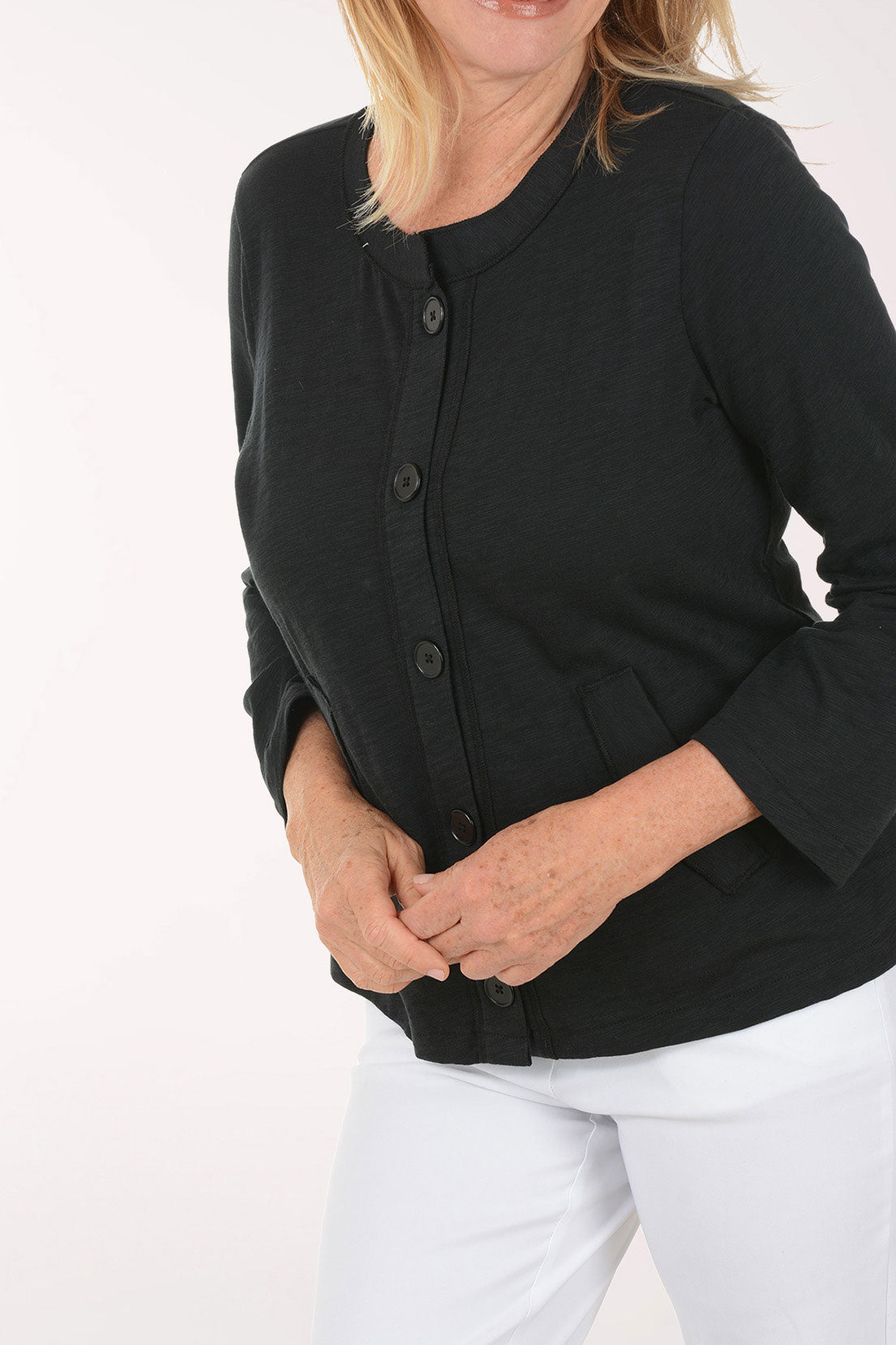 Woman wearing a black cardigan and white pants on a white background