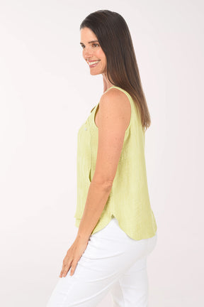 Woman wearing a light green sleeveless top and white pants on a white background