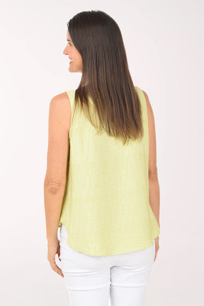 Woman wearing a light green sleeveless top and white pants on a white background