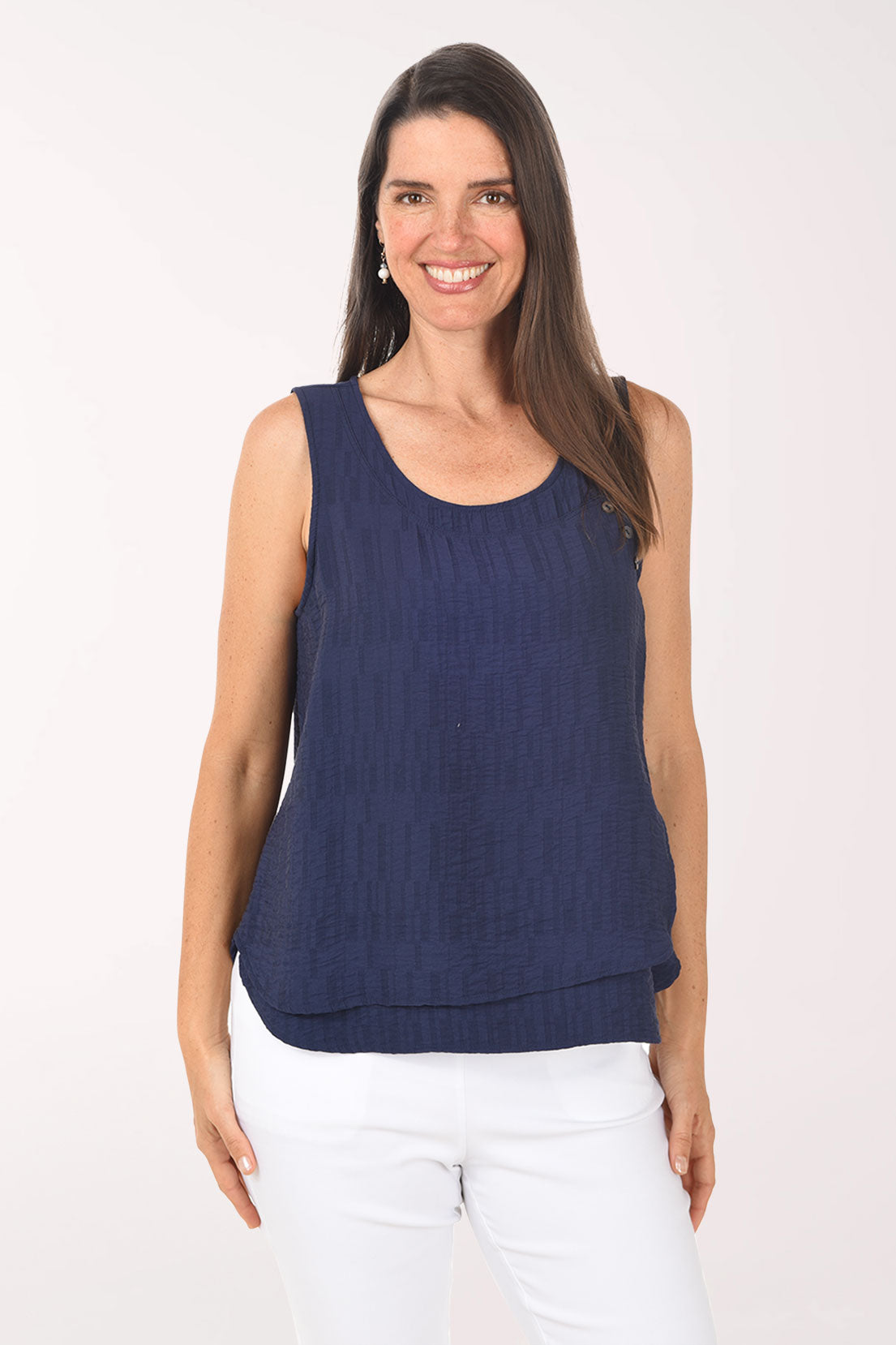 Woman wearing a navy sleeveless top and white pants on a white background