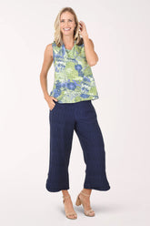 Woman wearing a sleeveless floral top and navy pants on a white background