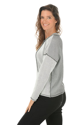 Woman wearing a gray patterned top with black stitching on a white background. Side shot.