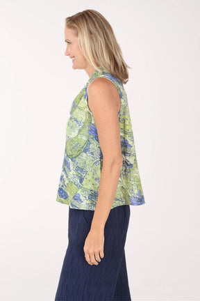 Woman wearing a sleeveless floral top and navy pants on a white background