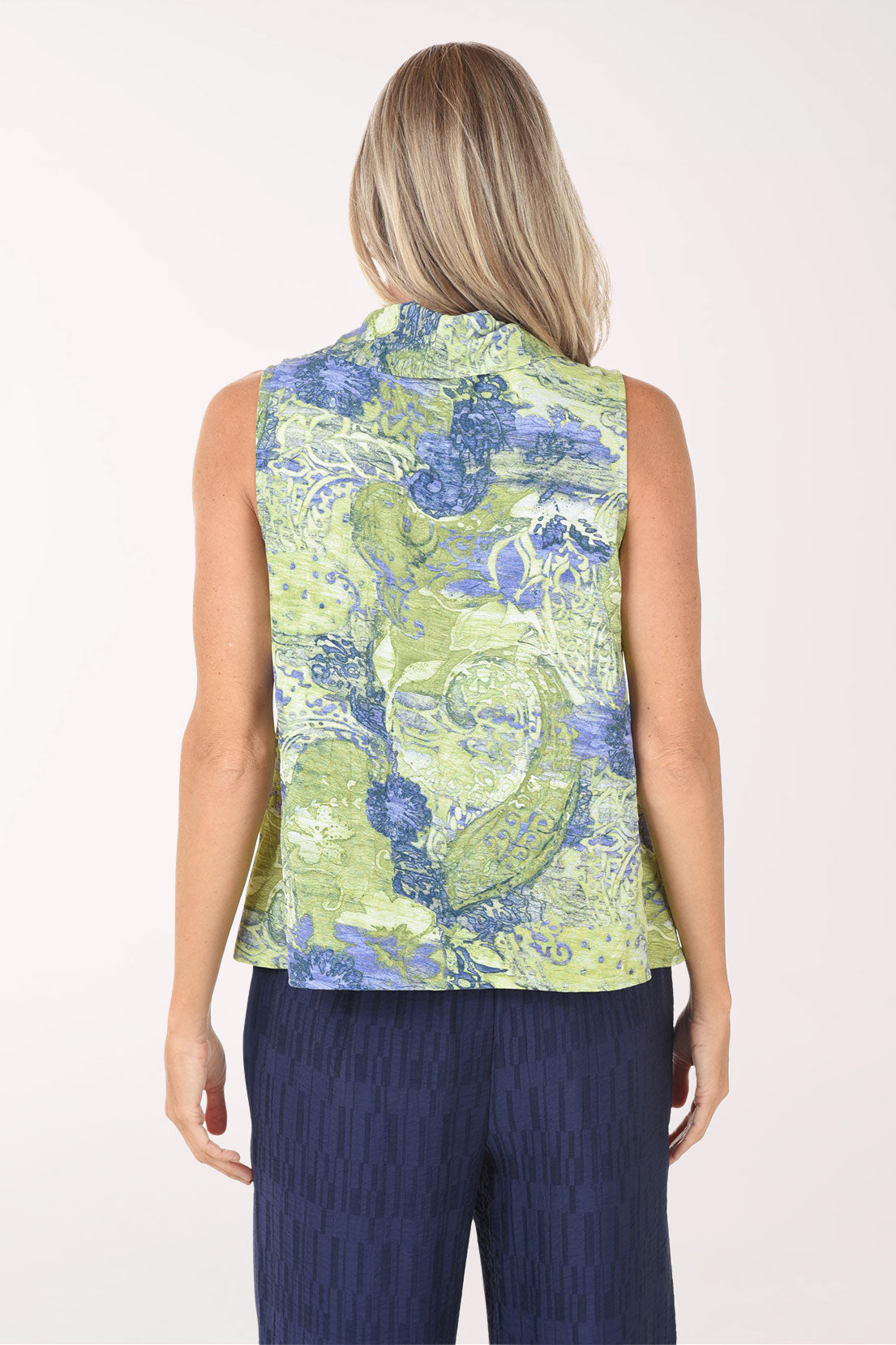 Woman wearing a sleeveless floral top and navy pants on a white background