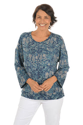 Woman wearing a blue paisley patterned top and white pants on a white background.
