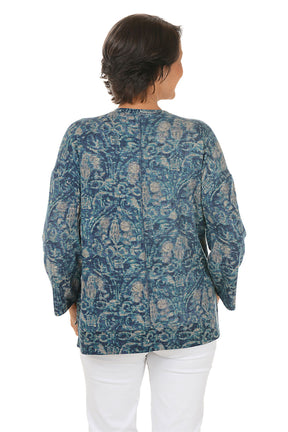 Woman wearing a blue paisley patterned top and white pants on a white background. Back shot.