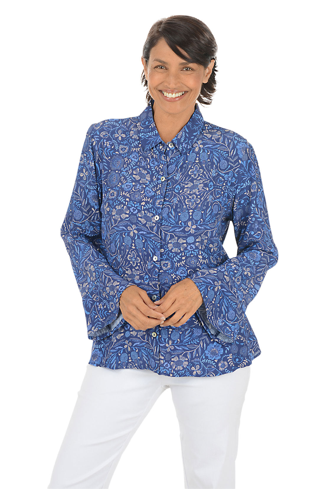 Woman wearing a blue patterned blouse and white pants on a white background.