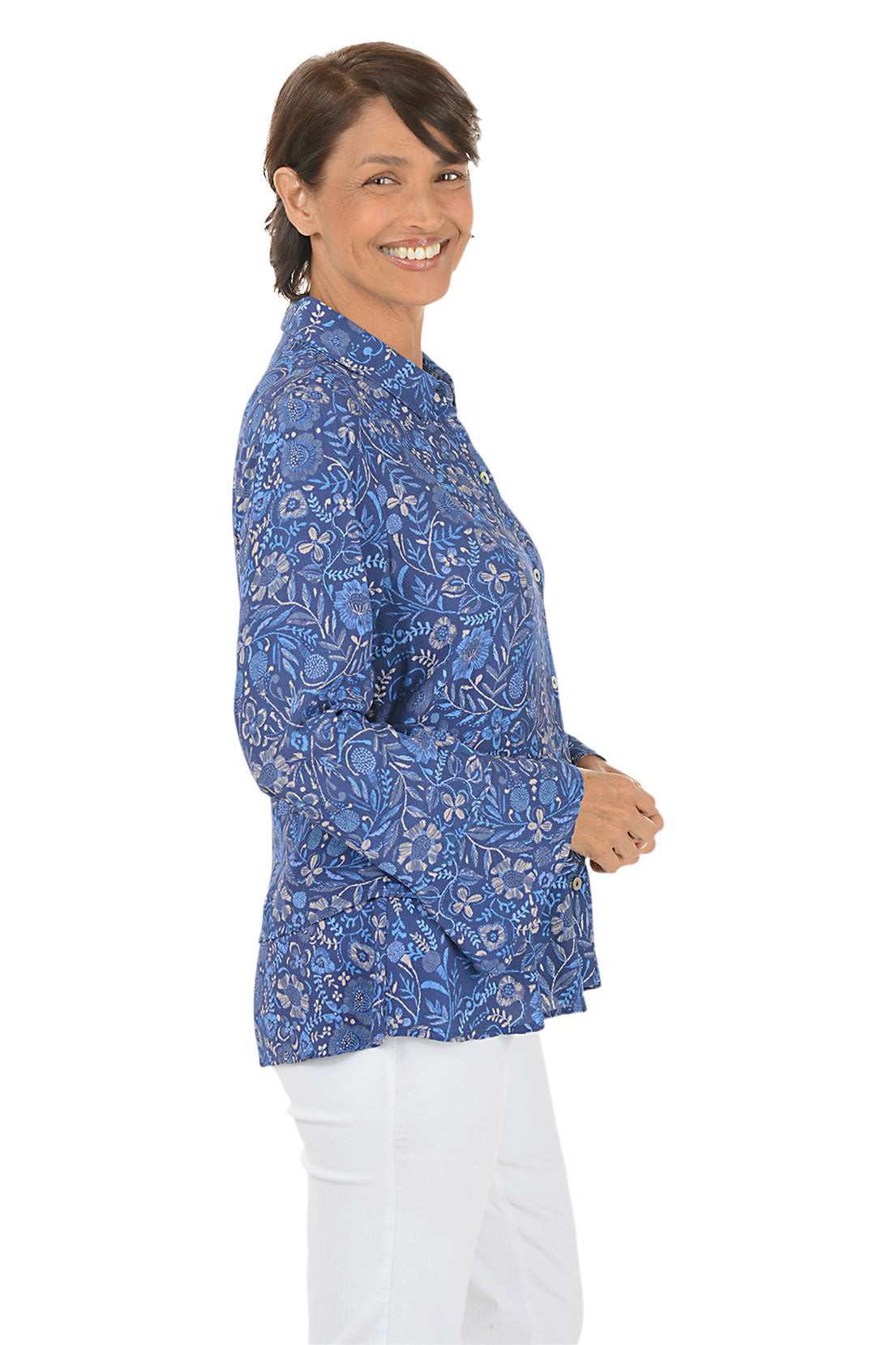 Woman wearing a blue patterned blouse and white pants on a white background. Side shot.