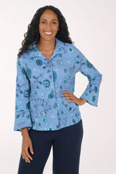 A woman modeling a light blue button-up shirt with a teal and dark blue floral paisley pattern, paired with dark navy pants, against a plain white studio background.