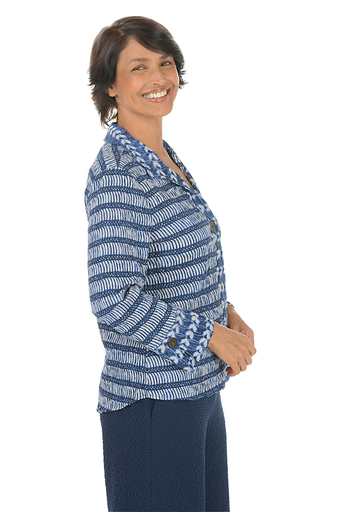 Woman wearing a blue patterned blouse on a white background. Side shot.