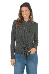 Woman wearing a black patterned shirt and blue jeans on a white background.