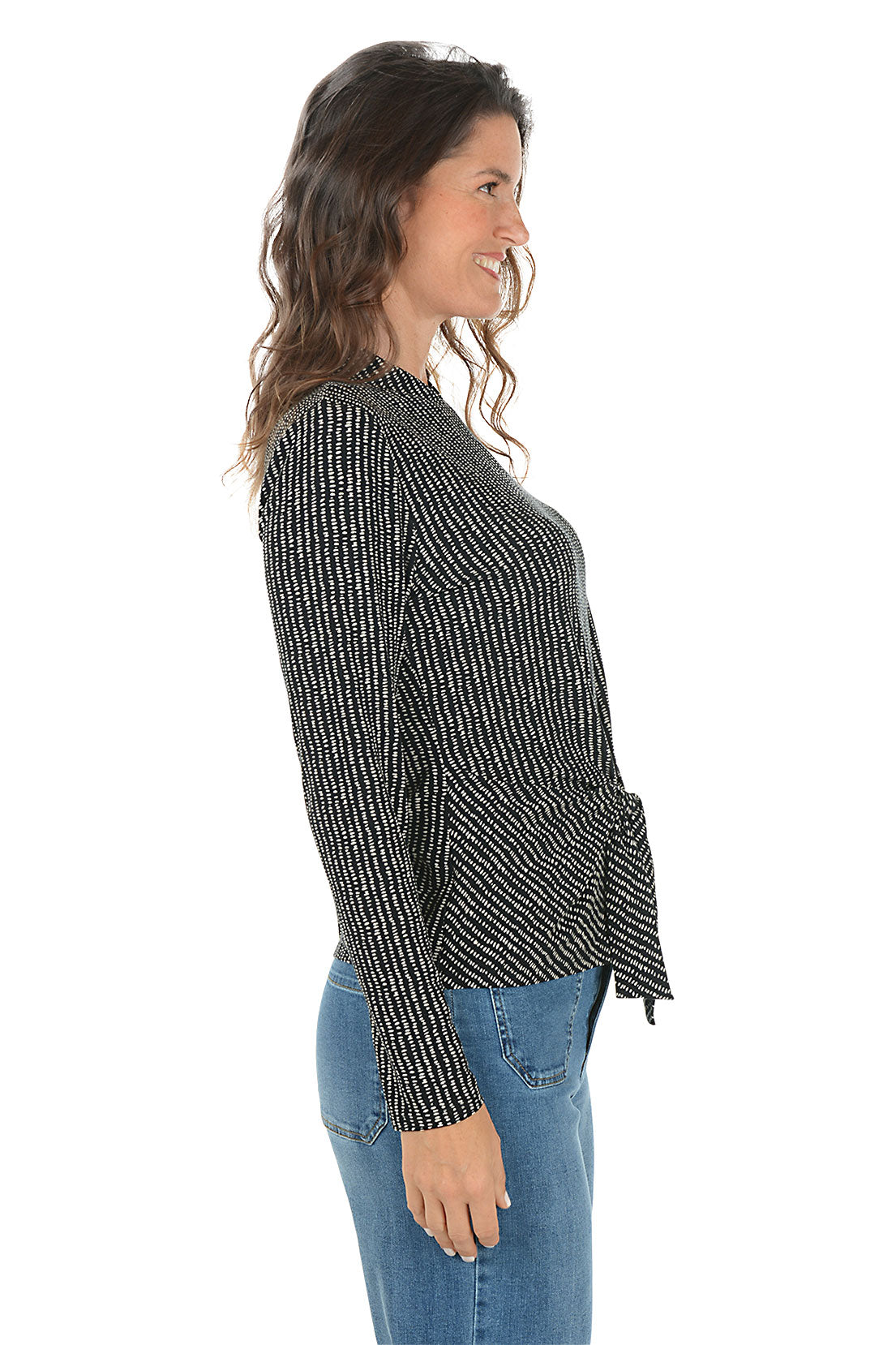 Woman wearing a black and white patterned blouse with blue jeans on a white background. Side shot.