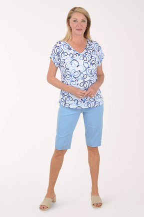 Woman wearing a blue and white patterned top with light blue shorts on a white background