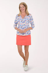 Woman wearing a colorful patterned top and coral skirt on a white background