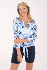 Woman wearing a blue floral blouse and navy shorts on a white background