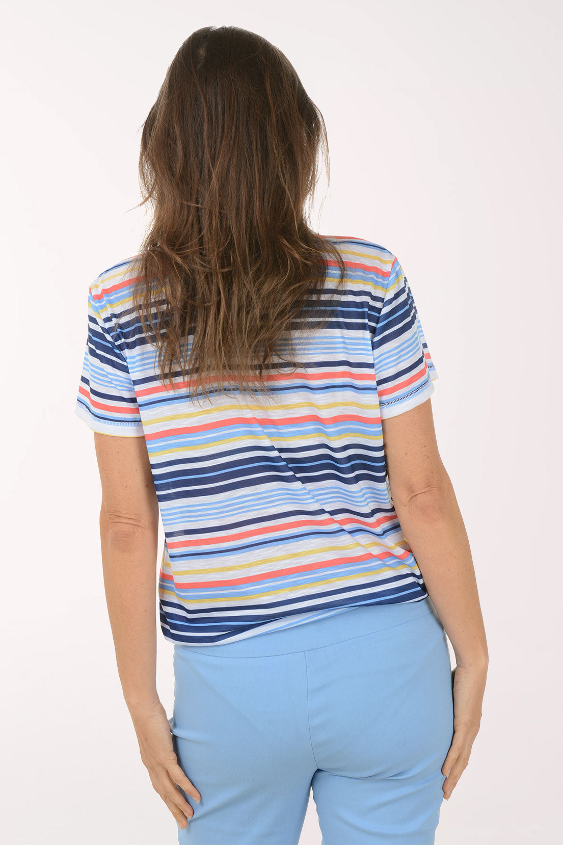Woman wearing a colorful striped polo shirt and light blue pants on a white background