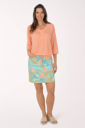 Woman wearing a peach blouse and colorful skirt on a white background