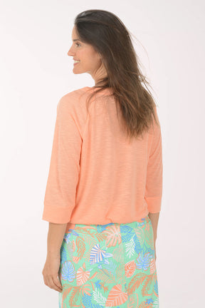 Woman wearing a peach-colored long-sleeve top with a floral skirt on a white background