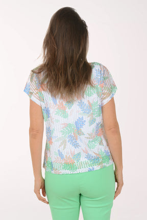 Woman wearing a colorful patterned top and green pants on a white background