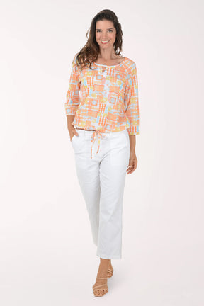 Woman wearing a patterned orange and white top with white pants on a white background