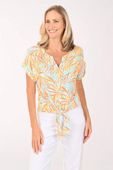 Woman wearing a short sleeve multi colored top with a tie detail on the hem.