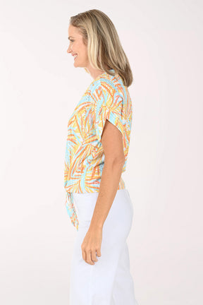 Woman wearing a short sleeve multi colored top with a tie detail on the hem.