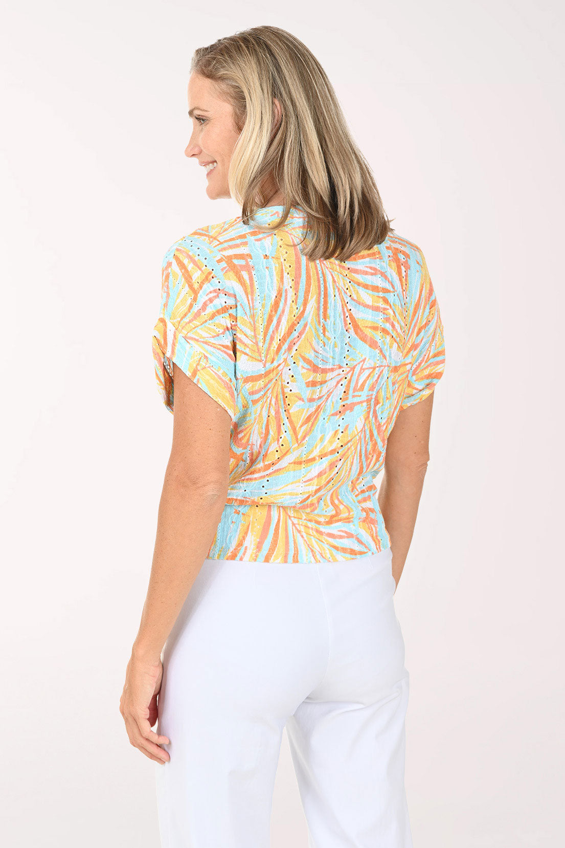 Woman wearing a short sleeve multi colored top with a tie detail on the hem.