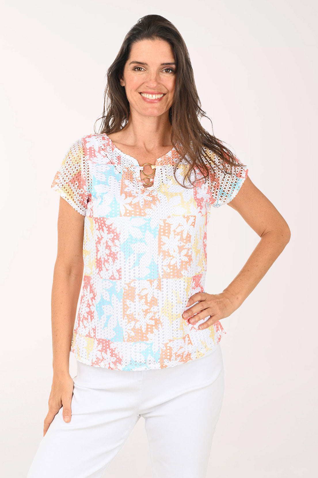Woman wearing a short sleeve multi colored top with a floral detail.
