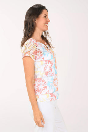 Woman wearing a short sleeve multi colored top with a floral detail.