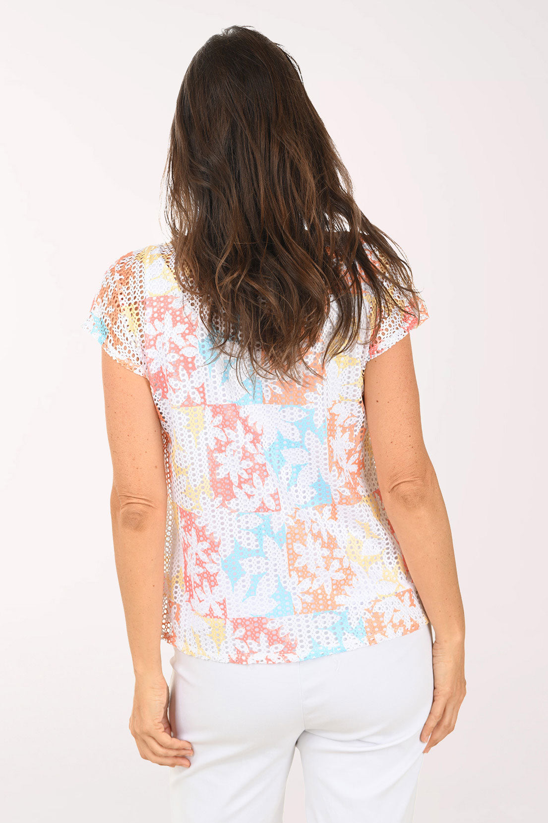 Woman wearing a short sleeve multi colored top with a floral detail.