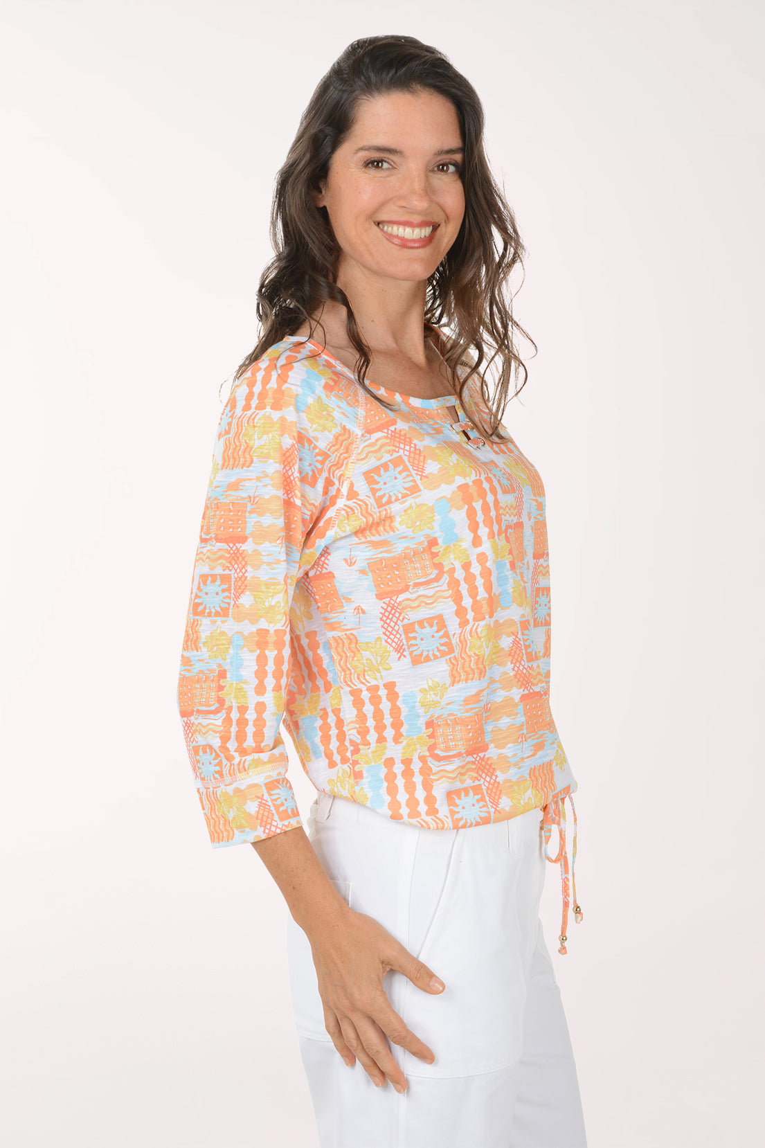 Woman wearing a colorful patterned top and white pants on a white background