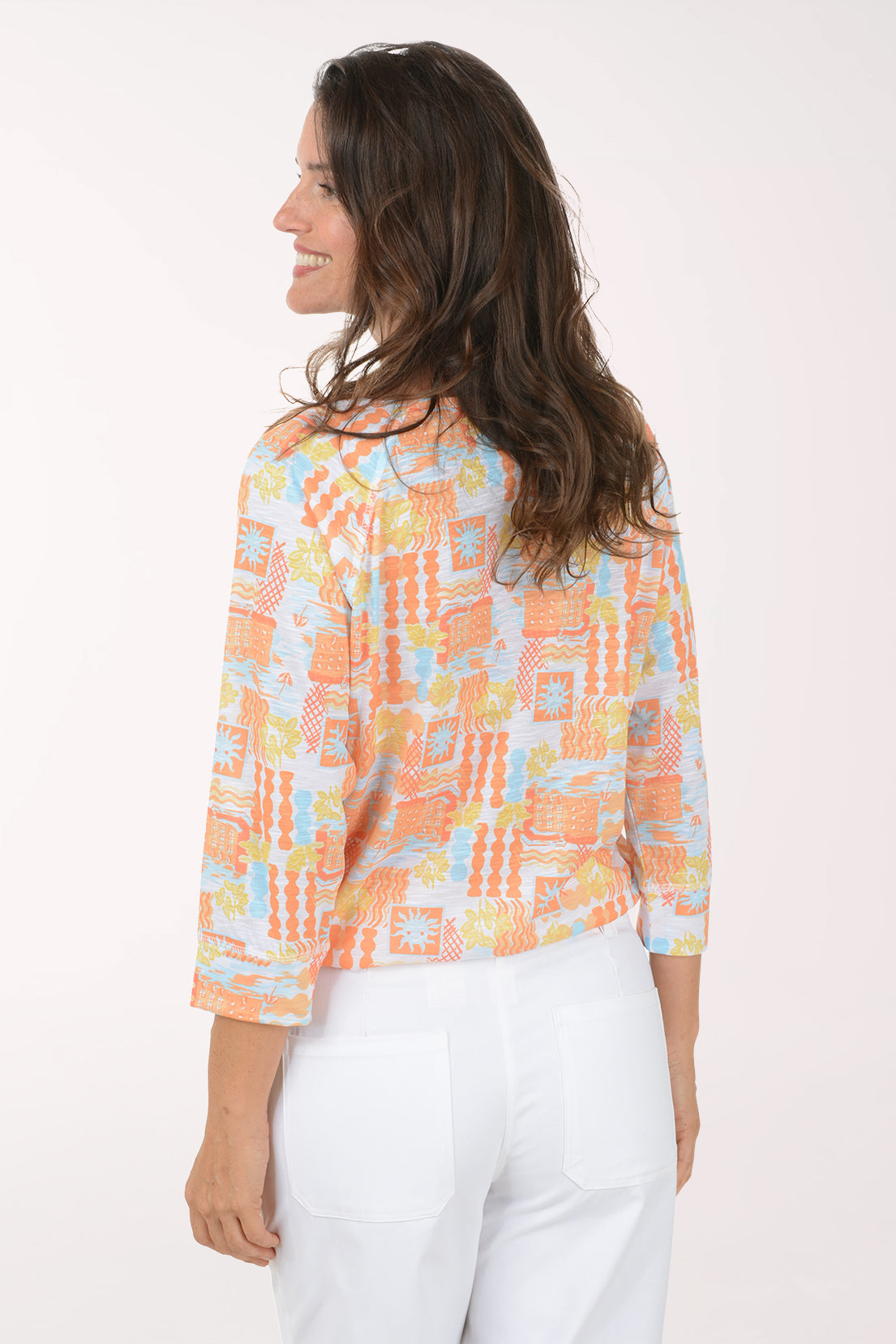 Woman wearing a colorful patterned top and white pants on a white background