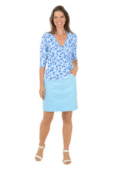 Woman wearing a blue floral top and light blue skirt on a white background.