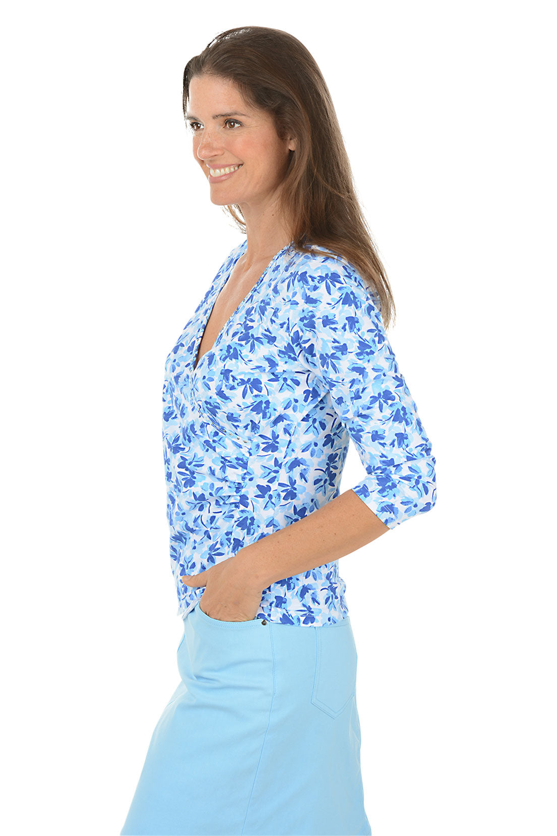 Woman wearing a blue floral blouse and light blue skirt on a white background. Side shot.