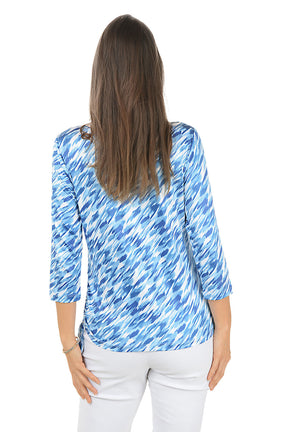 Woman wearing a blue patterned top with cut-out details on a white background. Back shot.