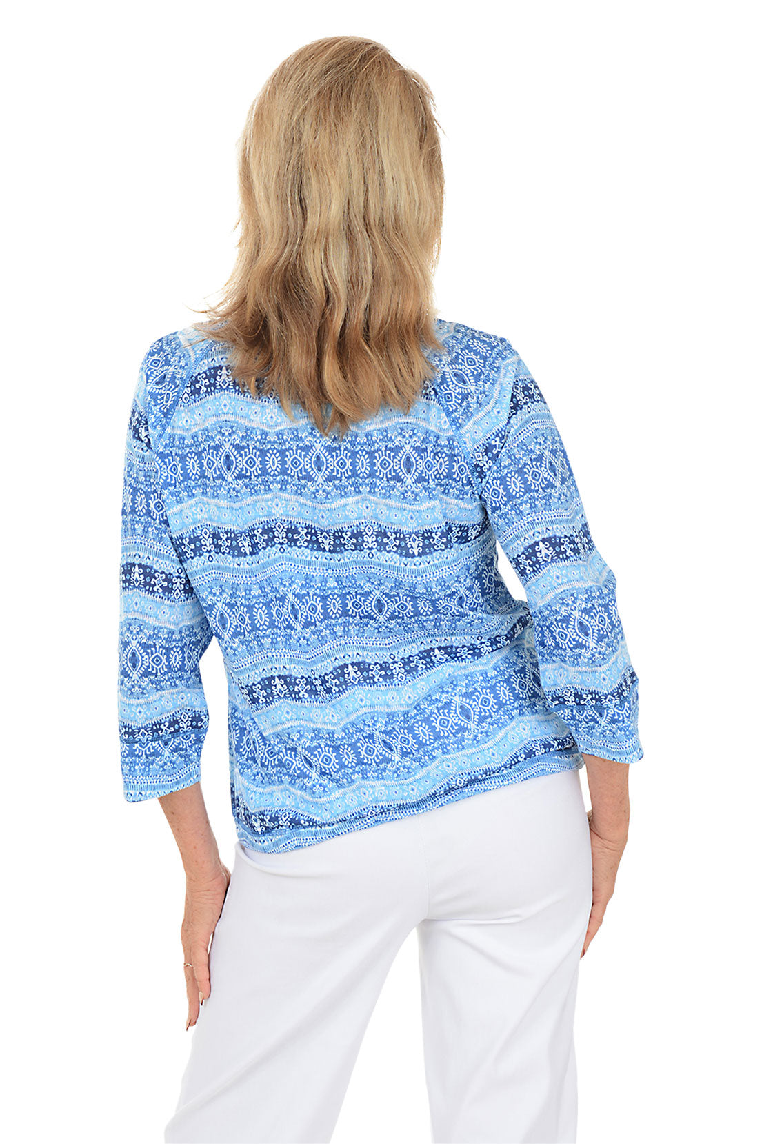 Woman wearing a blue patterned top and white pants on a white background. Back shot.