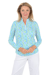 Woman wearing a patterned long-sleeve shirt and white pants on a white background.