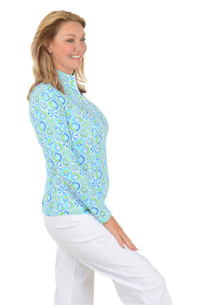 Woman wearing a patterned long-sleeve shirt and white pants on a white background. Side shot.