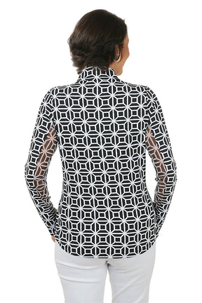 Woman wearing a black geometric patterned shirt with white pants on a white background