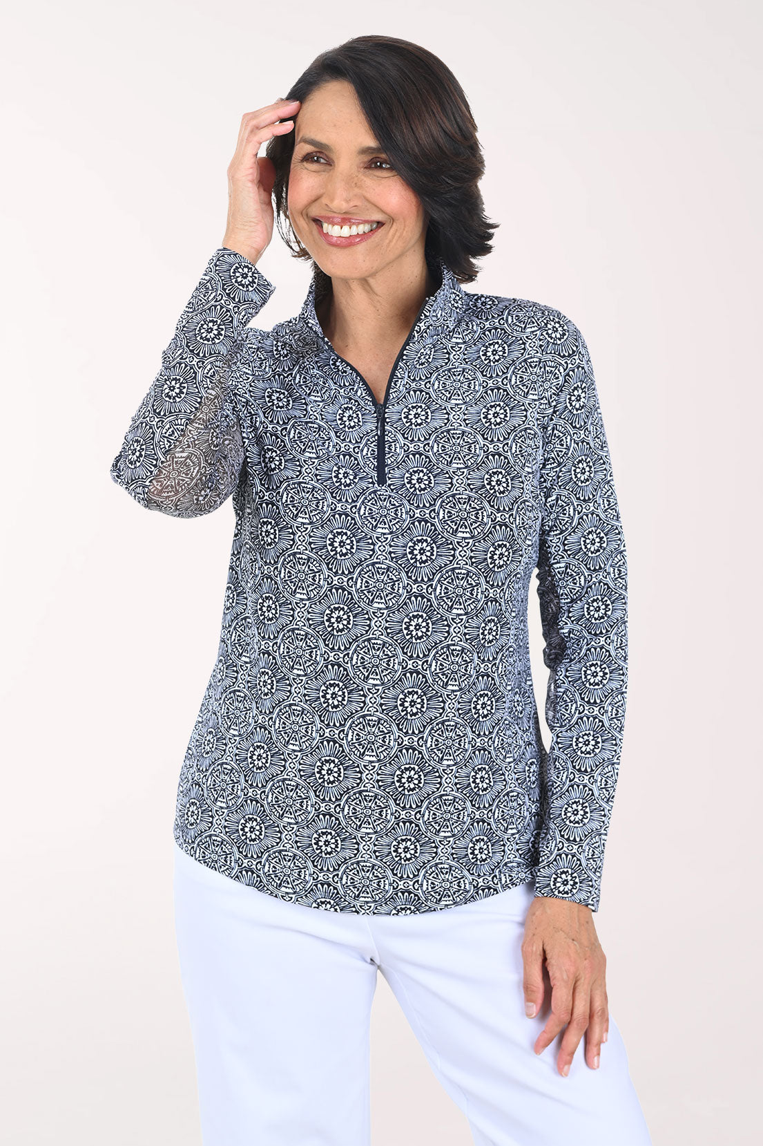 Woman wearing a patterned long-sleeve shirt and white pants on a plain background