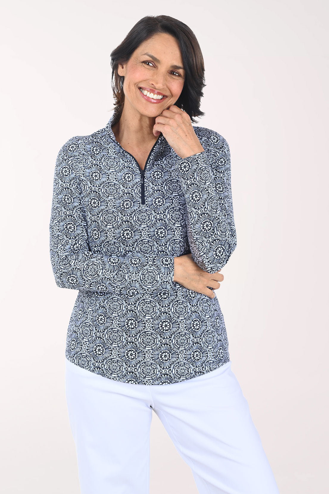 Woman wearing a patterned long-sleeve shirt and white pants on a plain background