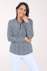 Woman wearing a patterned long-sleeve shirt and white pants on a plain background